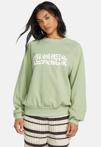 Lichtgroene sweatshirt met een geribbelde ronde hals en een oversized pasvorm. Voorzien van witte grafische tekst over de borst. Textuurstof.