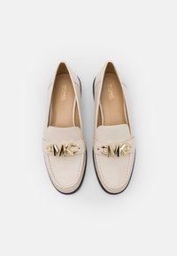 Mocassins en cuir beige avec un logo MK doré sur une bride, bout arrondi, et semelle en caoutchouc noire contrastante avec des coutures apparentes.