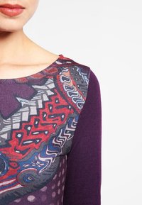 Getailleerde top met een levendige, veelkleurige patroon voorkant met geometrische ontwerpen op een paarse lange mouwen. Textuur, gebreid materiaal.