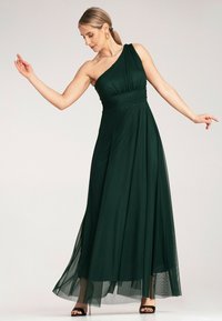 Długa, jednolita sukienka w ciemnozielonym kolorze, wykonana z lejącego materiału, z dopasowaną górą, drapowanym pasem i pełnym, warstwowym dołem.