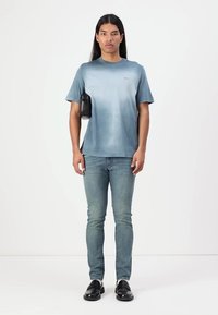 Kék átmenetes póló, pamutból készült, világos farmernadrággal párosítva. Fekete táska vállon, és fekete cipők egészítik ki az outfitet.