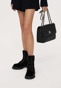 Black suede ankle boots with lace-up design, fuzzy lining, and thick rubber soles. Also features a black quilted handbag with chain strap.