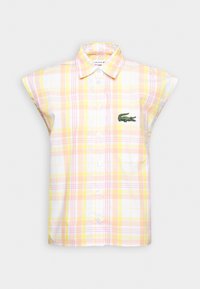 Chemise sans manches à boutons avec motif à carreaux jaune et rose et logo crocodile vert sur la poche poitrine sur fond blanc.