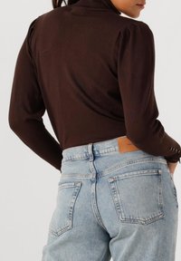 Bruine getailleerde trui met een hoge hals en opbollende schouders, gecombineerd met lichtblauwe hoge taille jeans met een leren label.