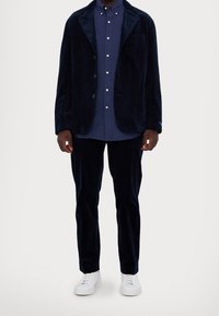 Marineblå kordflosshjälm med notch-lapel, matchad med en blå prickig skjorta och matchande byxor. Bärs med vita sneakers.