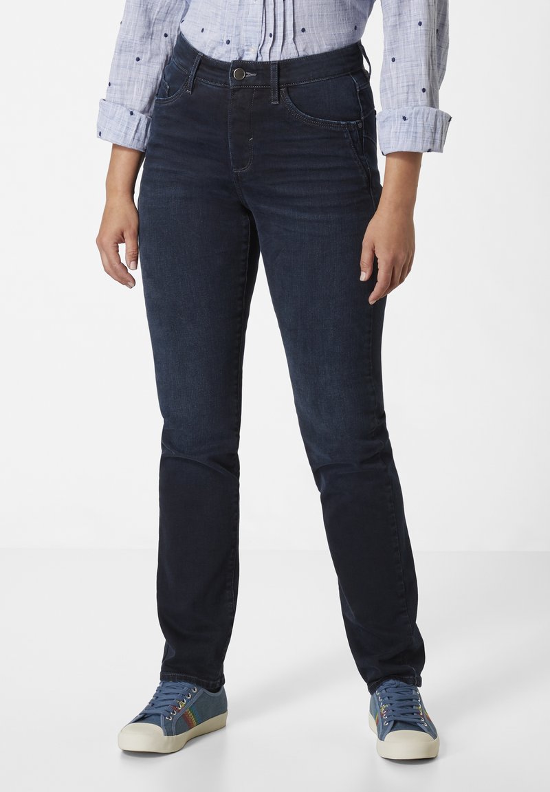 Dunkelblaue Jeans im Slim-Fit-Stil, mit Eingrifftaschen, Reißverschluss und flachem Bund. Getragen mit bunten Sneakern.