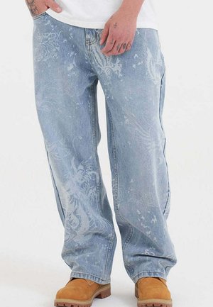 Hellblaue Jeans aus Denim mit lockerer Passform, die ein dezentes florales Muster aufweisen und mit brauen Schuhen getragen werden.