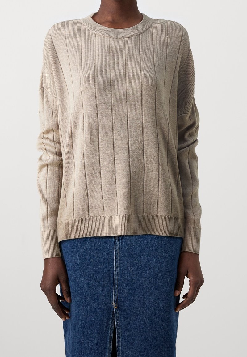 Beige ribbattuida neule, jossa on pyöreä kaula-aukko, pitkät hihat ja suora helma. Ominaisuuksiin kuuluvat pystysuorat raidat ja pehmeä rakenne. Yhdistetty farkkuhameeseen.