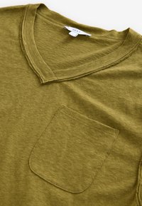 Olivgroen t-shirt met een V-hals, korte mouwen en een borstzakje. Zachte textuur met een subtiel gemêleerd patroon en zichtbare naden.