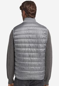 Szara, pikowana kamizelka z wysokim kołnierzem. Noszona na szarym, długim rękawie o gładkiej, błyszczącej fakturze.