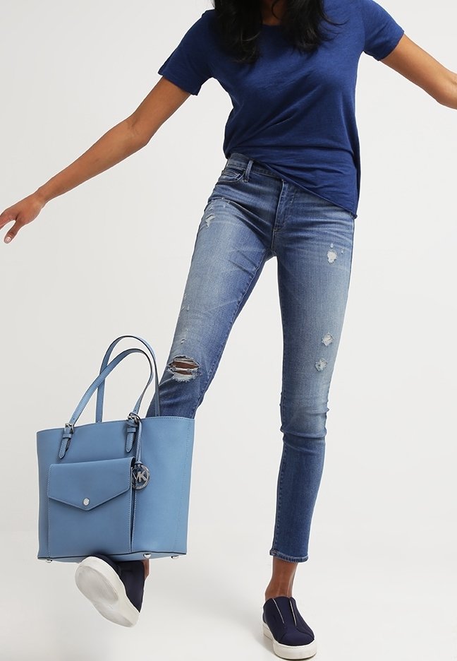 Sac fourre-tout bleu clair en cuir lisse avec une poche avant, une quincaillerie argentée et des poignées doubles ; porté avec un jean bleu délavé et des chaussures bleu marine.