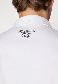 Hvit polo skjorte med en knappet krage og svart brodert tekst "Malbon Golf" på baksiden. Mykt stoff med en glatt tekstur.