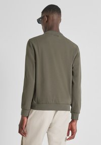 Sudadera ligera de color verde oliva con cuello redondo, puños y dobladillo acanalados; textura suave; marca visible en la parte posterior cerca del cuello.