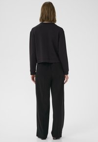 Svart kortärmad sweatshirt med lång ärm, slät textur, rund halsringning och en avslappnad passform, kombinerad med skräddarsydda svarta byxor.