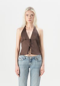 Top halter marrón hecho de tela de satén, con un escote en V profundo y un acento de lazo en la parte delantera. Combinado con unos vaqueros azules desgastados.