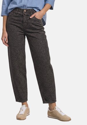 Personne portant un pantalon taille haute imprimé léopard gris foncé avec un bouton et une boucle, des baskets beiges et une chemise bleu clair.