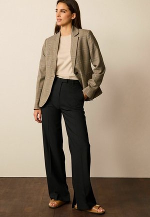 Lysternet ternet blazer i beige og brun, parret med en tætsiddende beige top og brede sorte bukser. Lysebrune sandaler fuldender looket.
