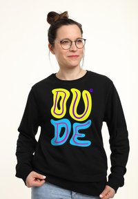 Felpa nera con testo audace e colorato "DUDE" in giallo, rosa e blu. Tessuto morbido con collo rotondo e maniche lunghe.