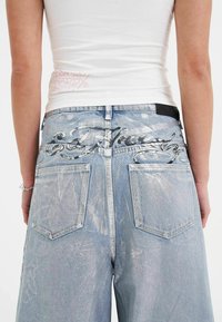 Lyseblå denimjeans med en blank finish, der har sølvmetallic broderi på baglommerne og et standard design til baglommerne.