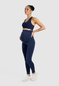 Granatowy zestaw sportowy ciążowy z biustonoszem i legginsami z elastycznego materiału. Charakteryzuje się wspierającym krojem z wysokim stanem i regulowanymi detalami.