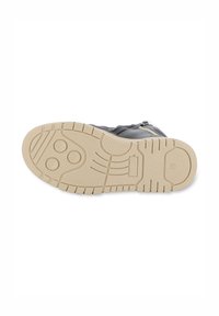 Chaussure grise avec une surface texturée, dotée d'une semelle en caoutchouc beige et de motifs de bande de roulement prononcés. Zip latéral pour un enfilage facile.