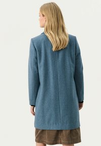 Blauer Wollmischungsmantel mit gerader Silhouette, taillierten Schultern und langen Ärmeln, mit einem Rückenschlitz und minimalen Nahtdetails.