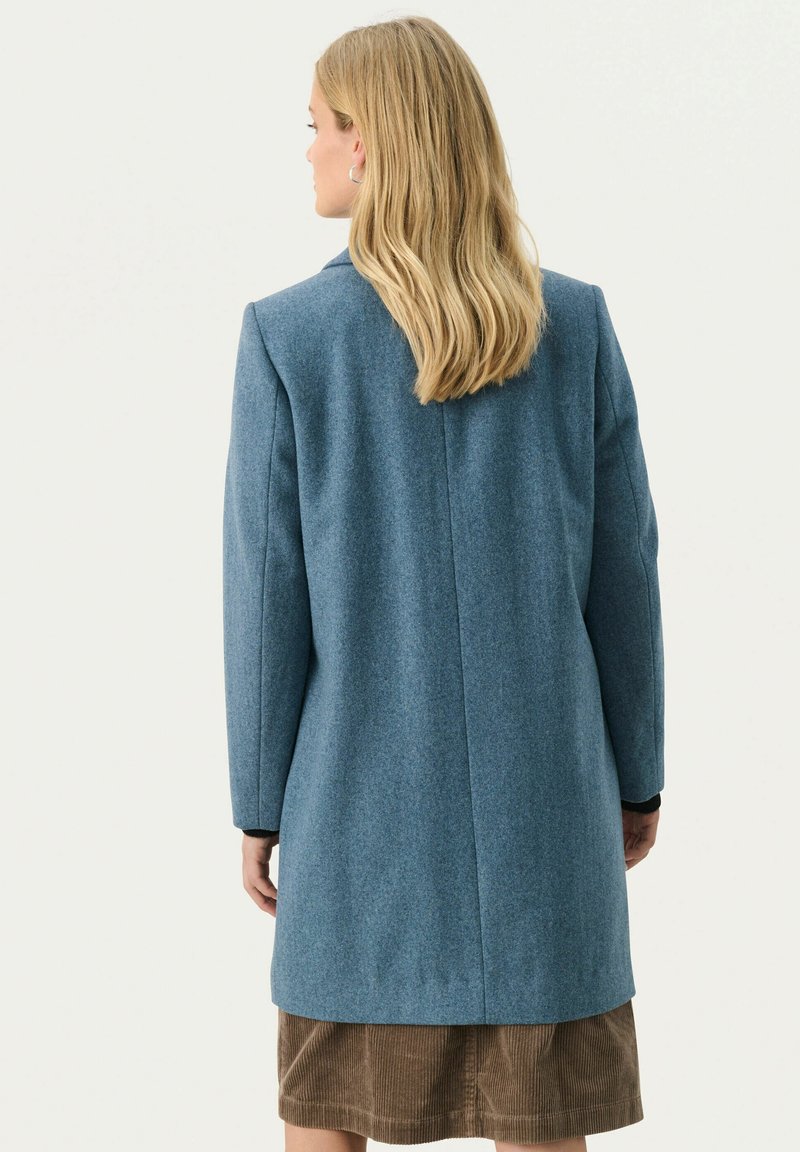 Niebieski płaszcz z mieszanki wełny o prostym kroju, z dopasowanymi ramionami i długimi rękawami, z rozcięciem z tyłu i minimalnymi detalami szycia.