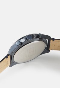 Montre en acier inoxydable noir avec une finition métallique lisse, dotée de boutons de chronographe et d'un bracelet en cuir. L'arrière est plat avec des gravures.