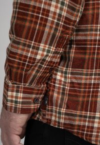 Bruine en oranje geruite flanellen overhemd met witte en groene accenten, met een knopenmanchet en een klein logo-label aan de zijkant.