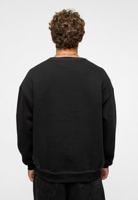Zwarte sweatshirt met een ronde hals, ribgebreide manchetten en zoom. Gelaagde stof met zichtbare stikdetails. Van achter bekeken.
