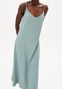Helles türkisfarbenes Kleid mit V-Ausschnitt und dünnen Trägern, aus einem glatten, fließenden Stoff. Verfügt über eine A-Linien-Form und dezente Drapierung.
