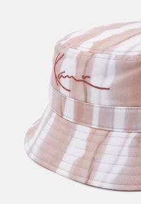 Cappello a secchiello in un motivo tie-dye rosa e bianco con dettaglio ricamato della firma. Realizzato in tessuto morbido con una corona arrotondata e una visiera rivolta verso il basso.