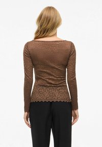 Bruine lange mouwen top met een getextureerd geribbeld patroon en een geschulpte zoom, gecombineerd met zwarte broek. De stof lijkt aansluitend te zijn.
