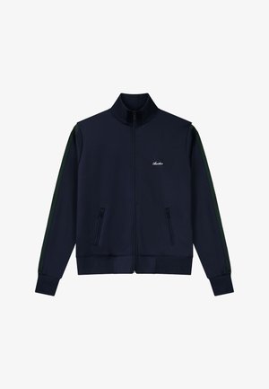 Tengerészkék, cipzáros kabát magas gallérral, fekete cipzáras zsebekkel, zöld csíkokkal az ujjak mentén és kis fehér logóval a bal mellrészen.