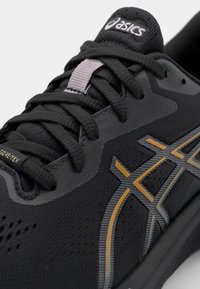 Black athletic shoe with textured upper, featuring gray and gold accents, lace closure, and a logo tag. Designed for comfort and durability.