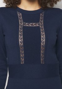 Navyblå stickad tröja med genomskinlig blommönsterdetalj och texturerade mönster fram, med ribbade accenter och rund halsringning.