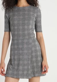 Vestido de manga corta con un patrón de cuadros en blanco y negro, que presenta un corsé ajustado y una falda acampanada. Hecho de tela texturizada.