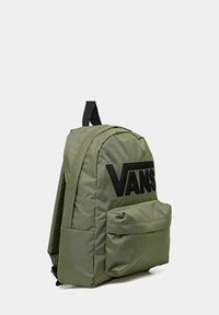 Zaino verde oliva realizzato in tessuto con forma arrotondata. Presenta un evidente logo nero "VANS" e una tasca frontale con pattina.