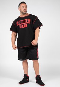 Black oversized t-shirt with red accents and "GORILLA WEAR" print, paired with black mesh shorts and black sneakers with red details.