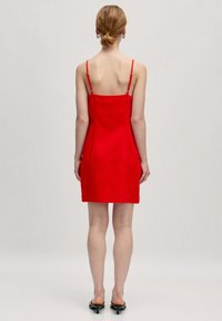 Rotes, figurbetontes Sommerkleid mit dünnen, verstellbaren Trägern, knielanger Schnitt, glatte Textur und minimalistisches Design. Verstellbares Rückendetail.