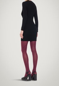 Musta ribbineuloksinen mekko, viininpunaiset kuvioidut sukkahousut ja massiiviset mustat korkosalot. Sukkahousuissa on geometrinen kuvio, joka tuo kontrastia tekstuuriin.