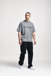 Camiseta gris de manga corta con "2Y STUDIOS" impreso en negrita negra. Combinada con pantalones negros de pierna recta y zapatillas blancas.