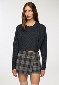 Maglione corto color navy con texture a treccia, abbinato a una mini gonna a quadretti. Il maglione presenta maniche lunghe e orlo a coste. Design classico.