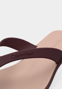 Κοντινό πλάνο μπεζ σανδάλι με σκούρα καφέ λουράκι που έχει ανάγλυφο το λογότυπο "Calvin Klein".