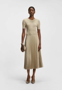 Knit midi-ikäpuu bežā krāsā ar īsām piedurknēm, krokotu satīna svārku un pieguļošu augšu. Apvienots ar mazu rokassomu un gludām bežām papēžkurpēm.