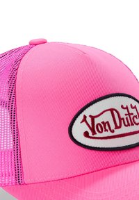 Casquette de camionneur rose avec un dos en mesh, portant un patch ovale blanc avec "Von Dutch" brodé en rouge. Tissu robuste, forme structurée.