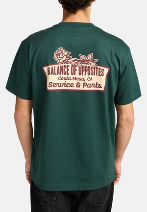 Groene katoenen t-shirt met een grafisch ontwerp op de achterkant met een roos en tekst: "Balans van Tegenstellingen, Costa Mesa, CA, Service & Broeken."