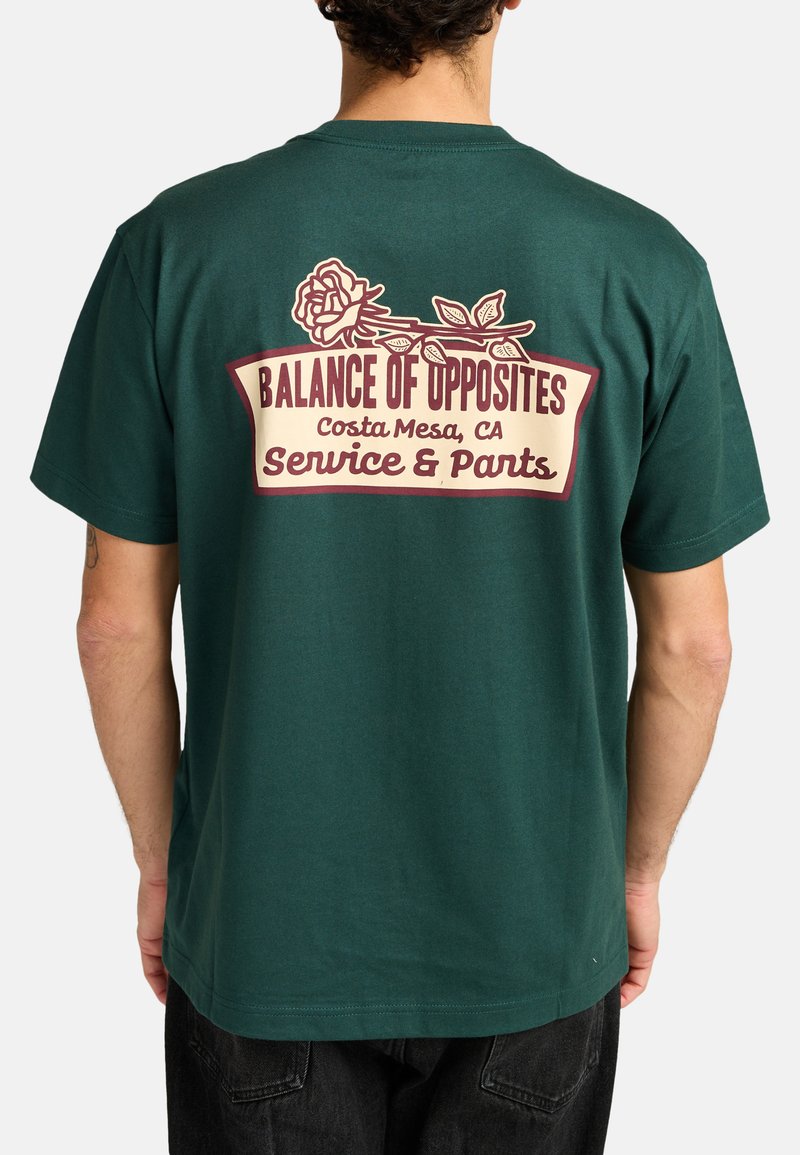 Camiseta de algodón verde con un gráfico en la parte posterior que incluye una rosa y el texto: "Balance de Opuestos, Costa Mesa, CA, Servicio y Pantalones."