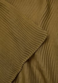 Tissu vert olive texturé avec de fines plis, affichant un matériau doux et léger et une bordure propre et cousue.