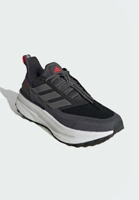 Black athletic shoe with a textured mesh upper, three gray stripes on the side, and a white cushioned sole; features red accents and laces.